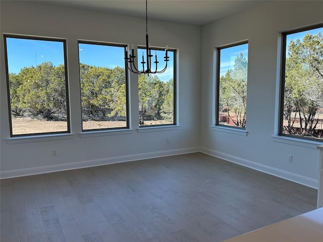 unfurnished dining area featuring a chandelier, dark wood-style flooring, and baseboards