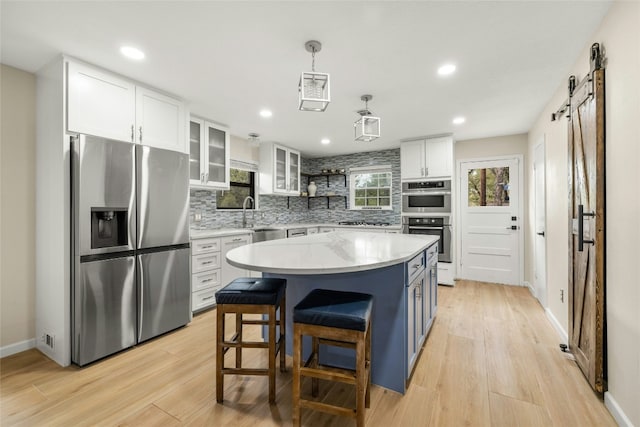 kitchen featuring white cabinets, a barn door, decorative light fixtures, a kitchen island, and stainless steel appliances