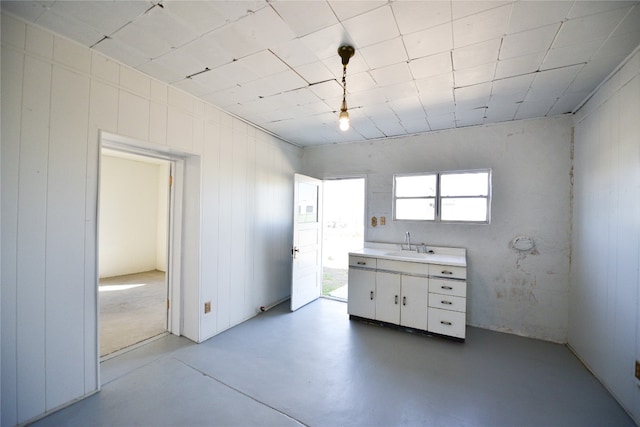 kitchen with finished concrete floors, white cabinetry, light countertops, and a sink