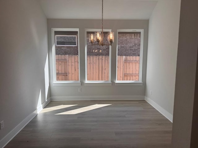 unfurnished dining area with wood finished floors, baseboards, and a chandelier