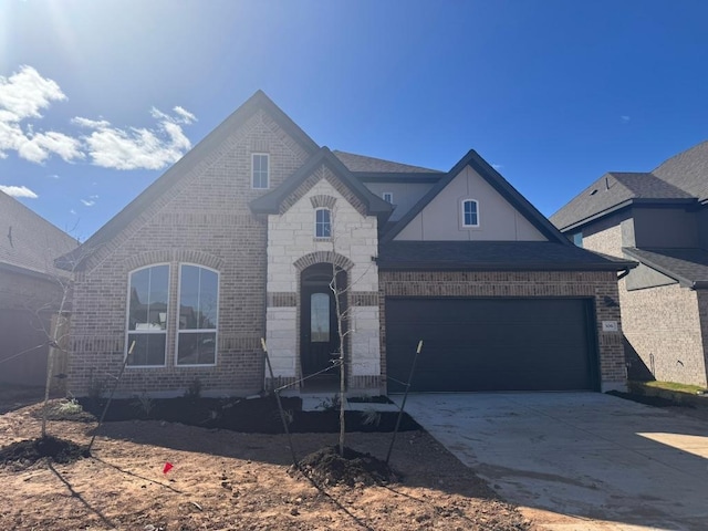 french country style house with brick siding, stone siding, concrete driveway, and a garage