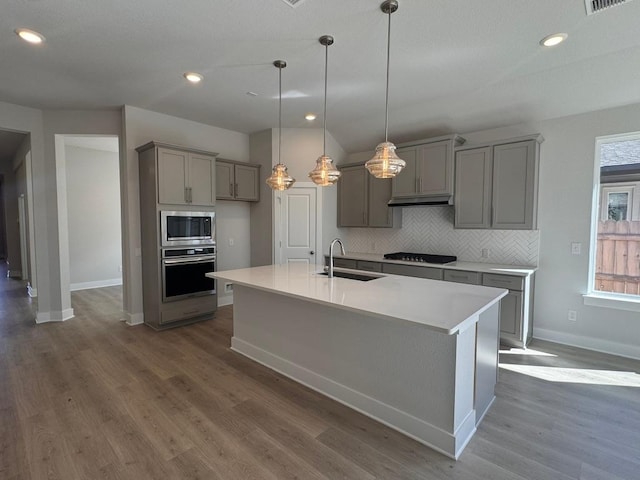 kitchen featuring gray cabinets, a sink, tasteful backsplash, stainless steel appliances, and dark wood-style flooring