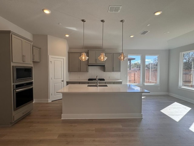 kitchen featuring stainless steel oven, visible vents, gray cabinets, and built in microwave