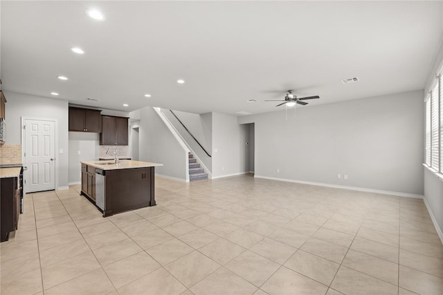 kitchen with dark brown cabinetry, ceiling fan, stainless steel dishwasher, backsplash, and an island with sink