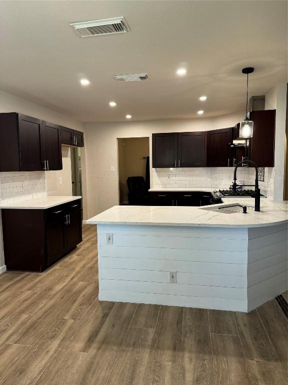 kitchen with visible vents, a peninsula, dark brown cabinets, and wood finished floors