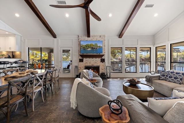 living room featuring vaulted ceiling with beams, ceiling fan, a wealth of natural light, and a brick fireplace