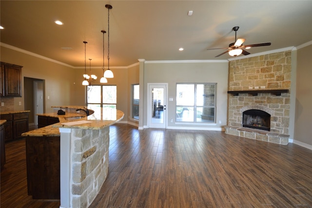 kitchen with light stone countertops, hanging light fixtures, dark wood-type flooring, a stone fireplace, and ornamental molding