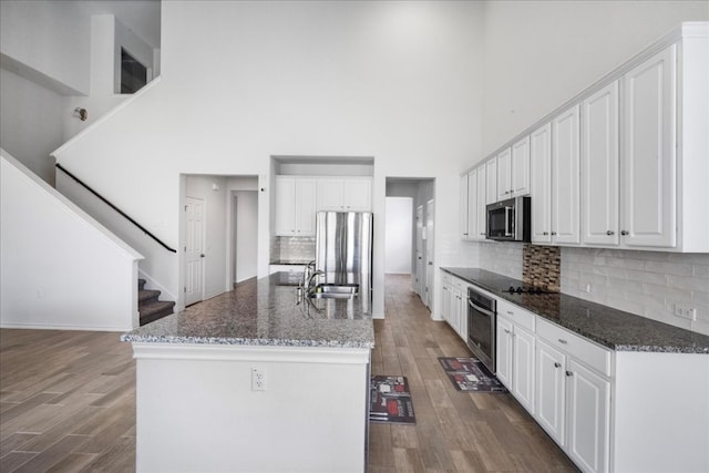 kitchen with white cabinets, appliances with stainless steel finishes, a towering ceiling, and dark hardwood / wood-style floors