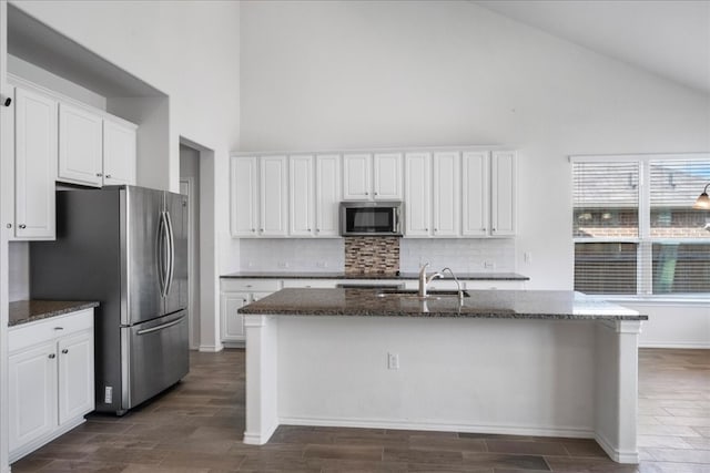 kitchen with appliances with stainless steel finishes, a kitchen island with sink, sink, dark stone countertops, and white cabinets