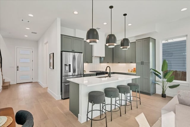 kitchen featuring sink, a kitchen breakfast bar, stainless steel refrigerator with ice dispenser, decorative backsplash, and decorative light fixtures