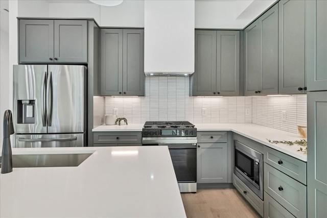 kitchen with appliances with stainless steel finishes, custom exhaust hood, light hardwood / wood-style flooring, and backsplash