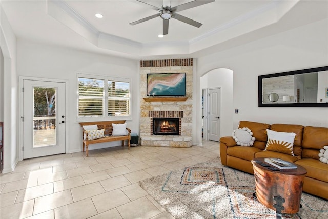 living room with ceiling fan, a tray ceiling, a fireplace, light tile patterned floors, and ornamental molding