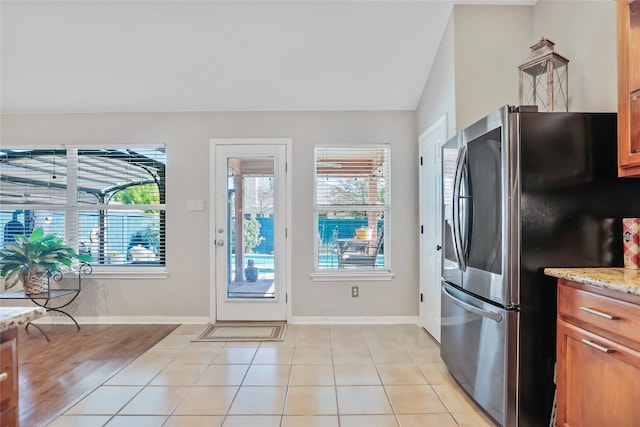 kitchen featuring stainless steel fridge, light tile patterned floors, vaulted ceiling, and a healthy amount of sunlight