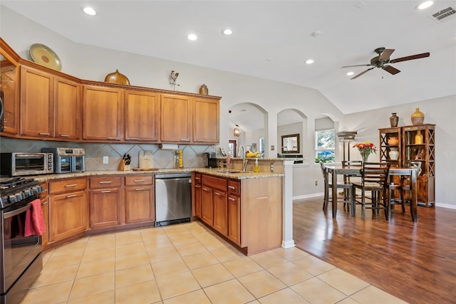 kitchen featuring kitchen peninsula, stainless steel dishwasher, light stone counters, black range with gas stovetop, and vaulted ceiling