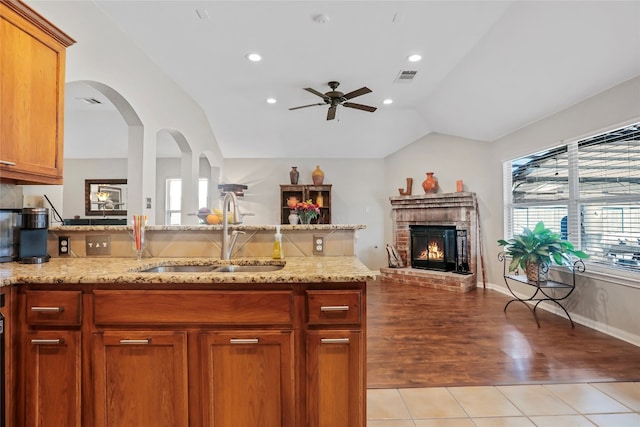 kitchen with lofted ceiling, sink, a brick fireplace, ceiling fan, and light hardwood / wood-style floors