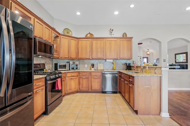 kitchen with sink, stainless steel appliances, light stone counters, kitchen peninsula, and lofted ceiling