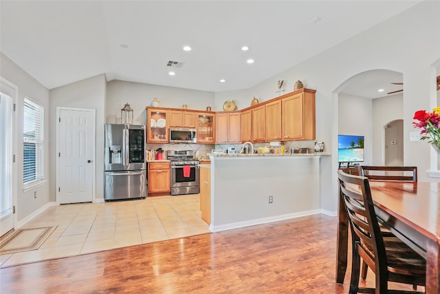 kitchen with ceiling fan, stainless steel appliances, tasteful backsplash, kitchen peninsula, and light wood-type flooring