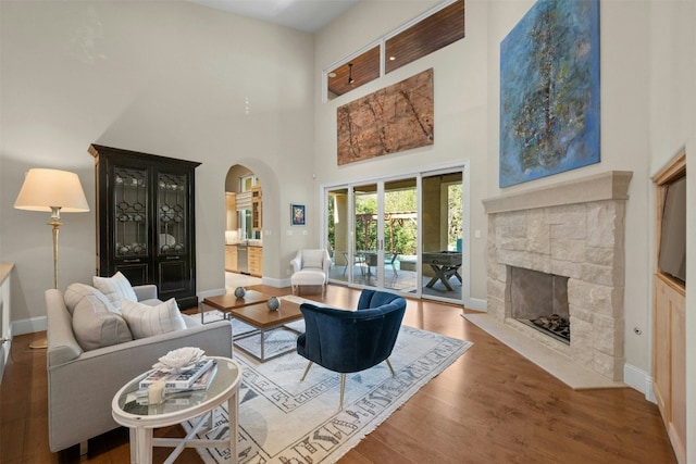 living room with a stone fireplace, wood-type flooring, and a high ceiling