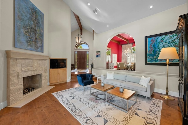 living room with a fireplace, lofted ceiling with beams, hardwood / wood-style flooring, and a notable chandelier