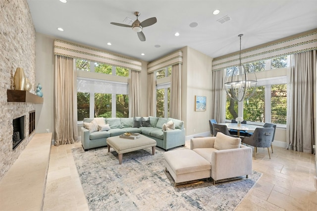 living room featuring a stone fireplace and ceiling fan with notable chandelier