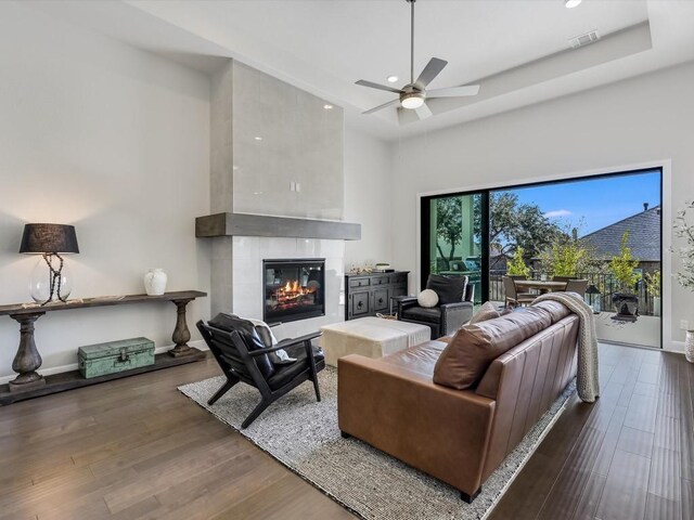 living room featuring ceiling fan, a large fireplace, a high ceiling, and dark hardwood / wood-style floors