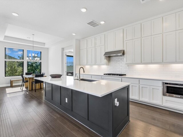 kitchen with hanging light fixtures, dark hardwood / wood-style floors, an island with sink, appliances with stainless steel finishes, and white cabinetry