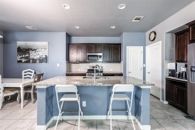 kitchen featuring stainless steel appliances, light stone counters, a kitchen island with sink, and sink