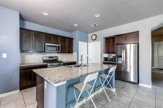 kitchen with a kitchen bar, dark brown cabinetry, stainless steel appliances, sink, and a center island with sink