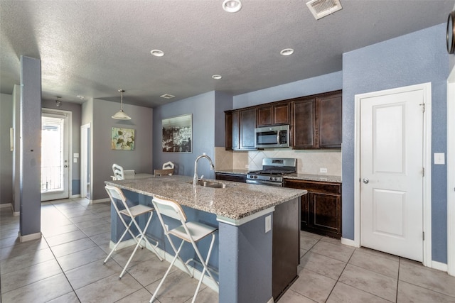 kitchen featuring a center island with sink, a kitchen breakfast bar, sink, light stone countertops, and appliances with stainless steel finishes