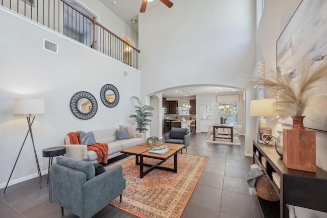 living room with ceiling fan, dark tile patterned flooring, and a towering ceiling