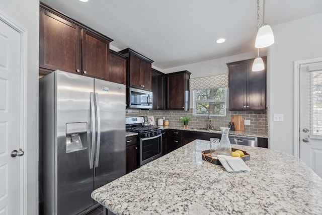 kitchen featuring pendant lighting, appliances with stainless steel finishes, sink, light stone counters, and a center island