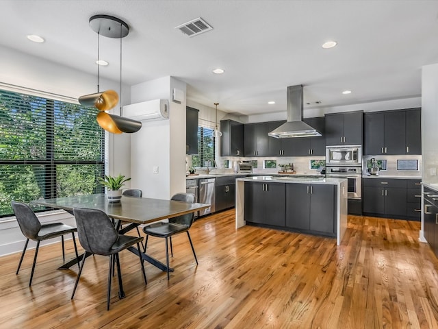 kitchen featuring pendant lighting, wall chimney range hood, a kitchen island, appliances with stainless steel finishes, and light hardwood / wood-style floors