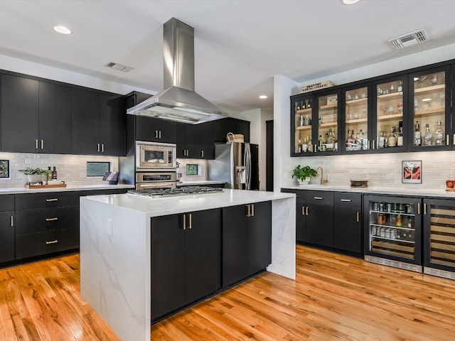 kitchen featuring a center island, extractor fan, light hardwood / wood-style floors, stainless steel appliances, and beverage cooler