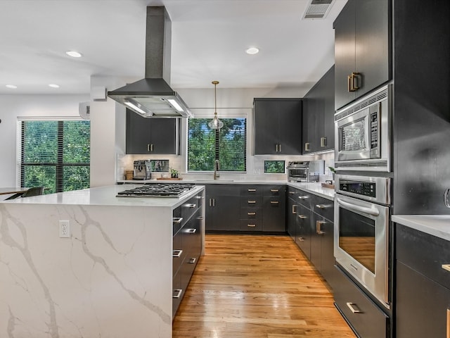 kitchen with tasteful backsplash, decorative light fixtures, light hardwood / wood-style floors, island exhaust hood, and stainless steel appliances