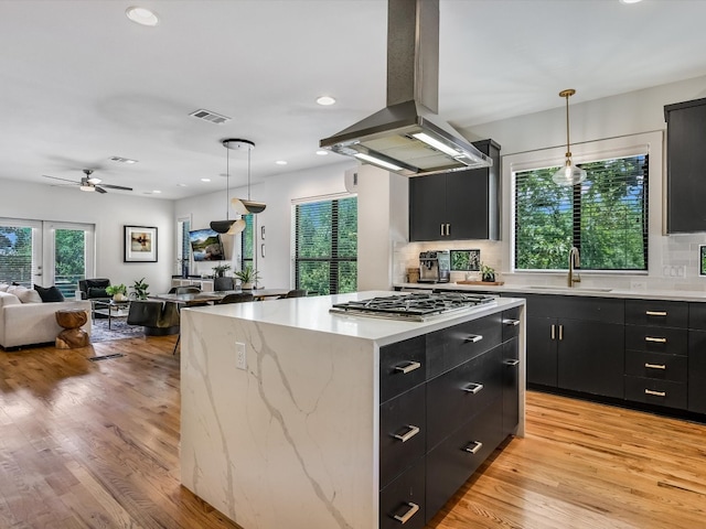 kitchen featuring sink, hanging light fixtures, a kitchen island, light wood-type flooring, and island range hood