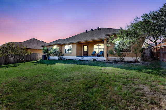 back house at dusk featuring cooling unit, a patio, and a lawn