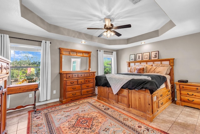 tiled bedroom with ceiling fan and a tray ceiling