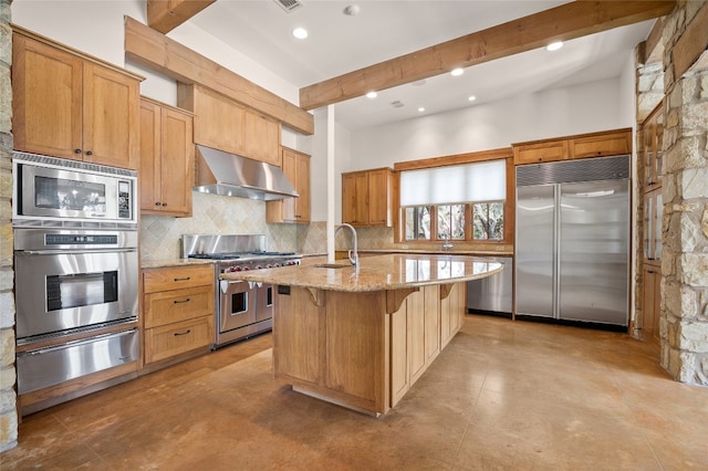 kitchen featuring beam ceiling, built in appliances, a center island with sink, and wall chimney range hood