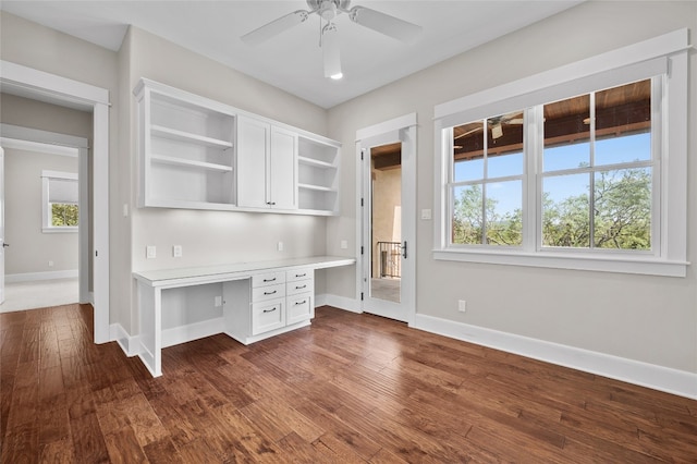 unfurnished office with dark hardwood / wood-style floors, ceiling fan, and built in desk