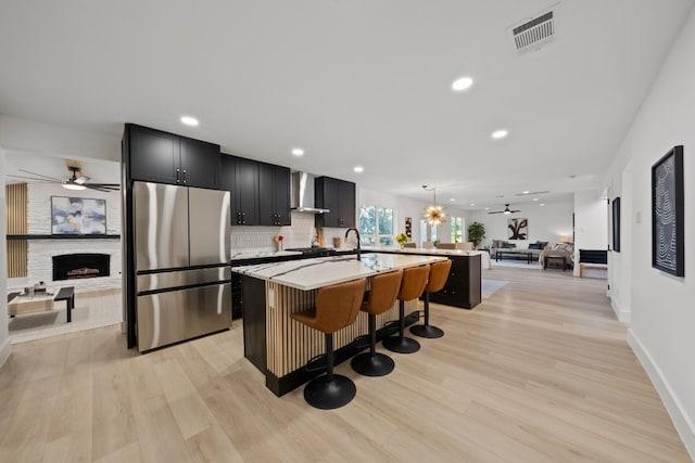 kitchen with wall chimney range hood, stainless steel fridge, pendant lighting, a kitchen bar, and a center island with sink