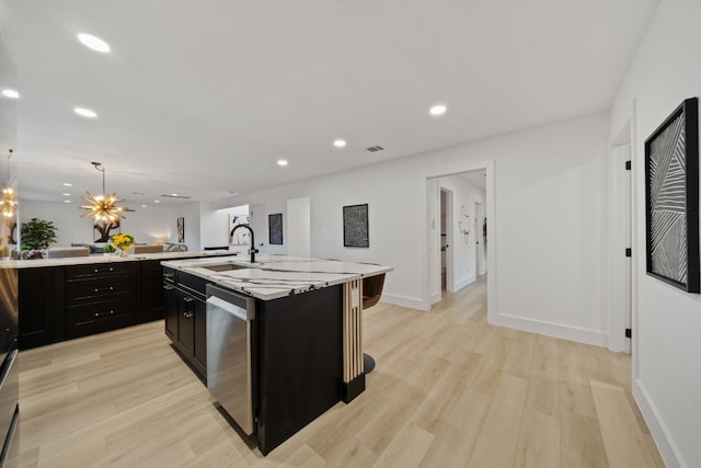 kitchen with light hardwood / wood-style flooring, stainless steel dishwasher, an island with sink, decorative light fixtures, and a kitchen bar