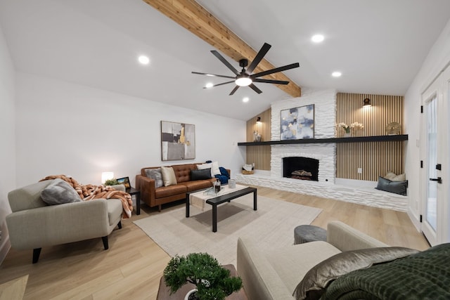 living room featuring a stone fireplace, ceiling fan, light hardwood / wood-style flooring, and lofted ceiling with beams