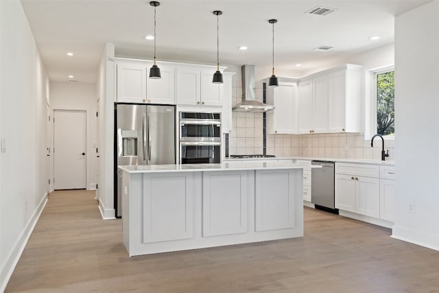 kitchen featuring a center island, wall chimney range hood, appliances with stainless steel finishes, light hardwood / wood-style floors, and white cabinetry