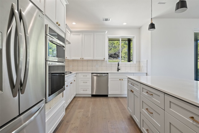 kitchen featuring white cabinetry, light hardwood / wood-style flooring, backsplash, decorative light fixtures, and appliances with stainless steel finishes