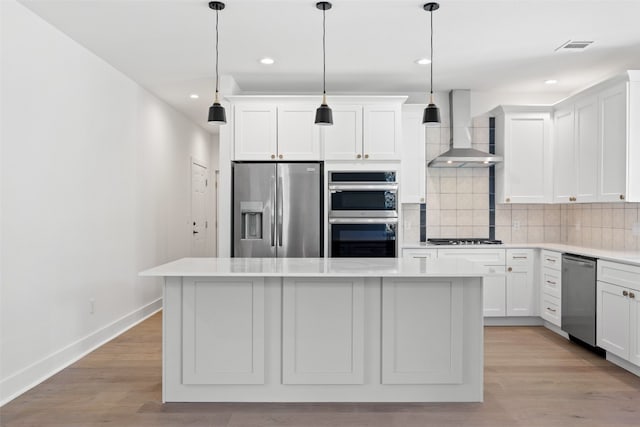 kitchen with a center island, hanging light fixtures, wall chimney exhaust hood, and stainless steel appliances