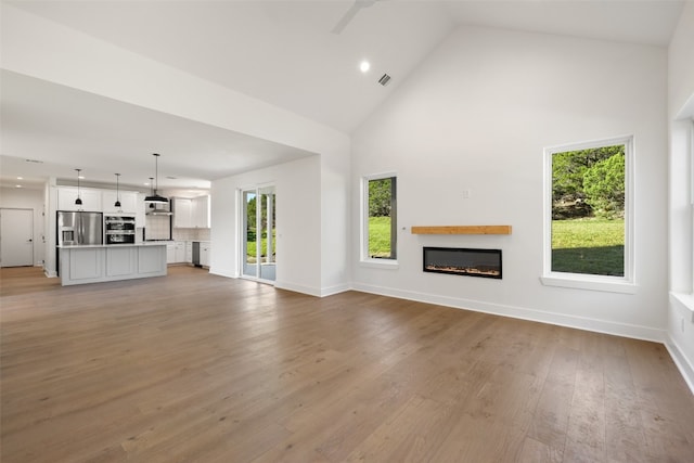 unfurnished living room with high vaulted ceiling and light wood-type flooring