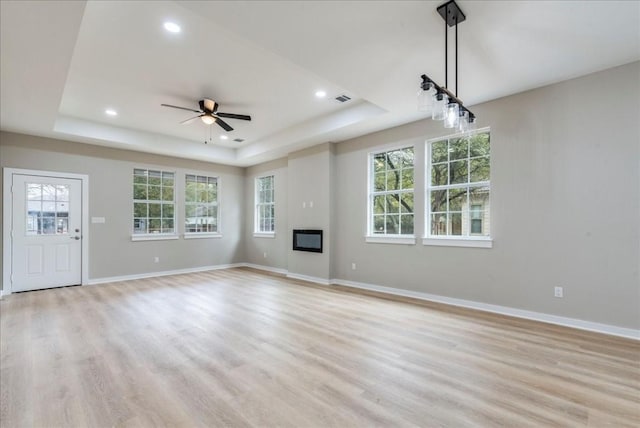 unfurnished living room with ceiling fan, a raised ceiling, and light hardwood / wood-style flooring