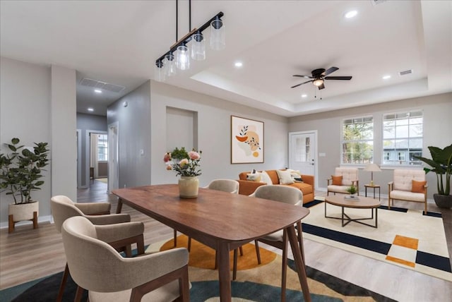 dining area with ceiling fan, a tray ceiling, and light hardwood / wood-style flooring