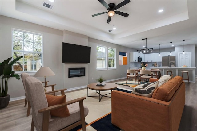 living room with light hardwood / wood-style floors, a raised ceiling, ceiling fan, and a healthy amount of sunlight