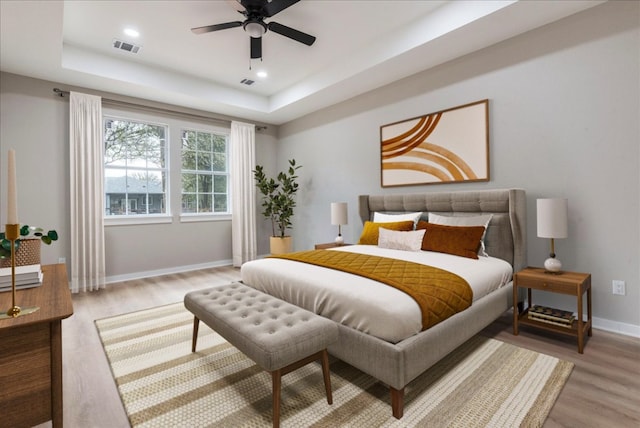 bedroom with ceiling fan, a raised ceiling, and light hardwood / wood-style flooring